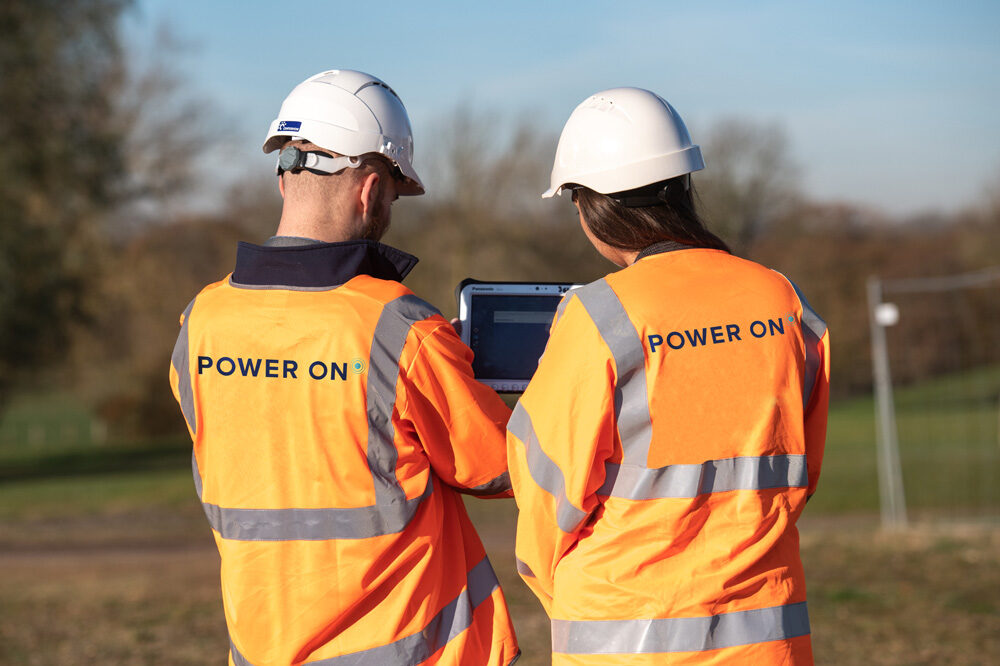 Two people in a high vis and a hard hat looking at a tablet