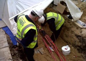 View down into a trench where two construction workers are working on a red cable.